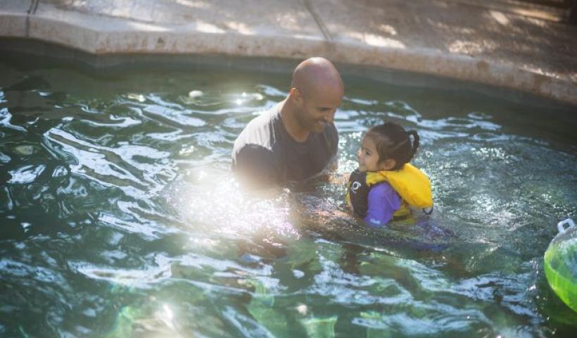 Man and child in life vest swimming in pool.