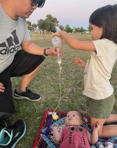 Father and older child work together to feed baby via NG tube
