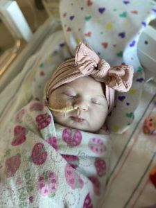 Sleeping baby wrapped in ladybug blanket, pink bow on head and NG tube