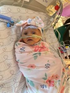 Infant wrapped in flower blanket with medical tubes visible and bow on head