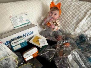 Baby with orange bow on head, surrounded by NG supplies