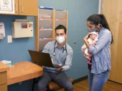 Masked provider and mother with newborn in exam room