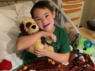 Boy in hospital bed, hugging stuffed dog
