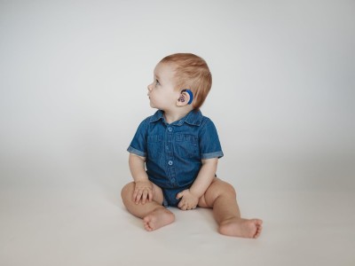 Infant sitting on floor showing hearing aid on left ear