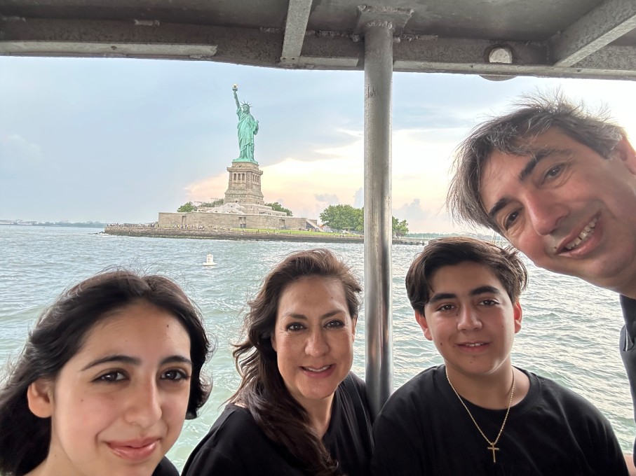 Teen boy, teen girl and parents smiling in front of Statue of Liberty